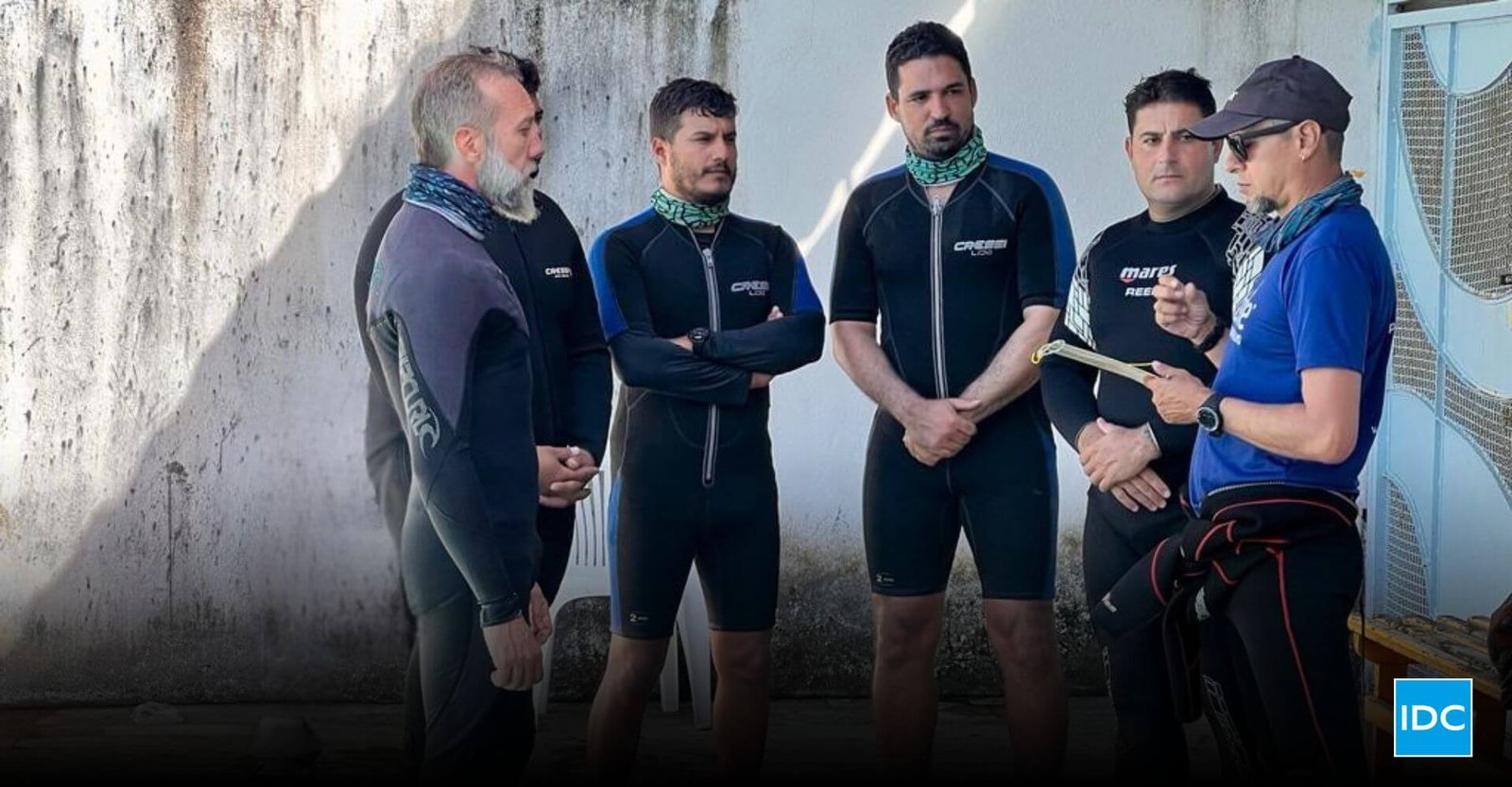 Confident scuba diving instructor leading a dive briefing with students before entering the water, representing leadership in the competitive dive instructor job market.