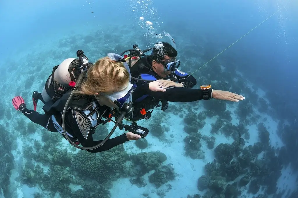 IDC student and instructor practice underwater navigation skills while scuba diving over a coral reef.