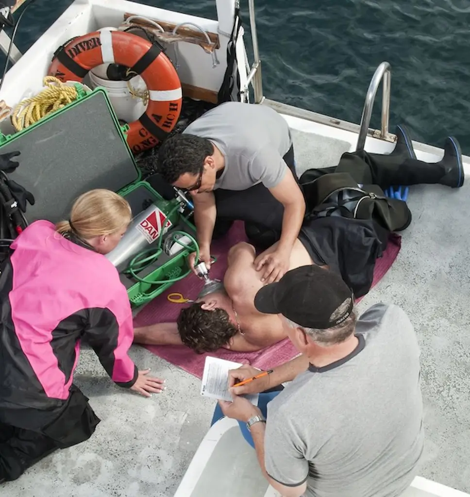 Emergency oxygen provider administers oxygen to a person lying on the deck of a boat while three other responders assist